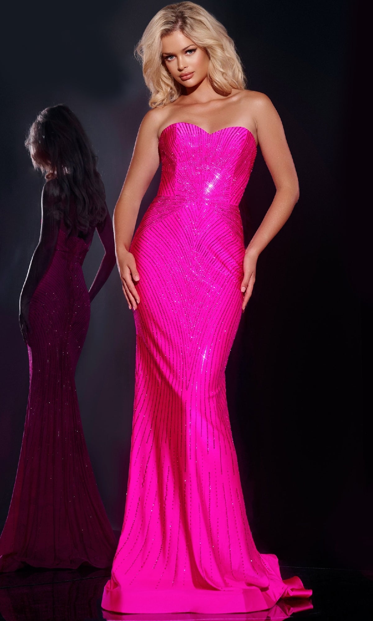 A woman faces forward in the Jovani 38655 long prom dress featuring a strapless sweetheart neckline and sparkly embellishments; her reflection appears behind her against a dark background.